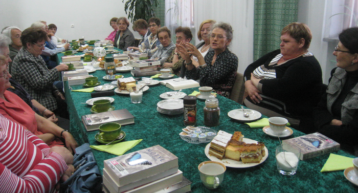 Spotkanie klubu, członkinie i członkowie przy stole z poczęstunkiem